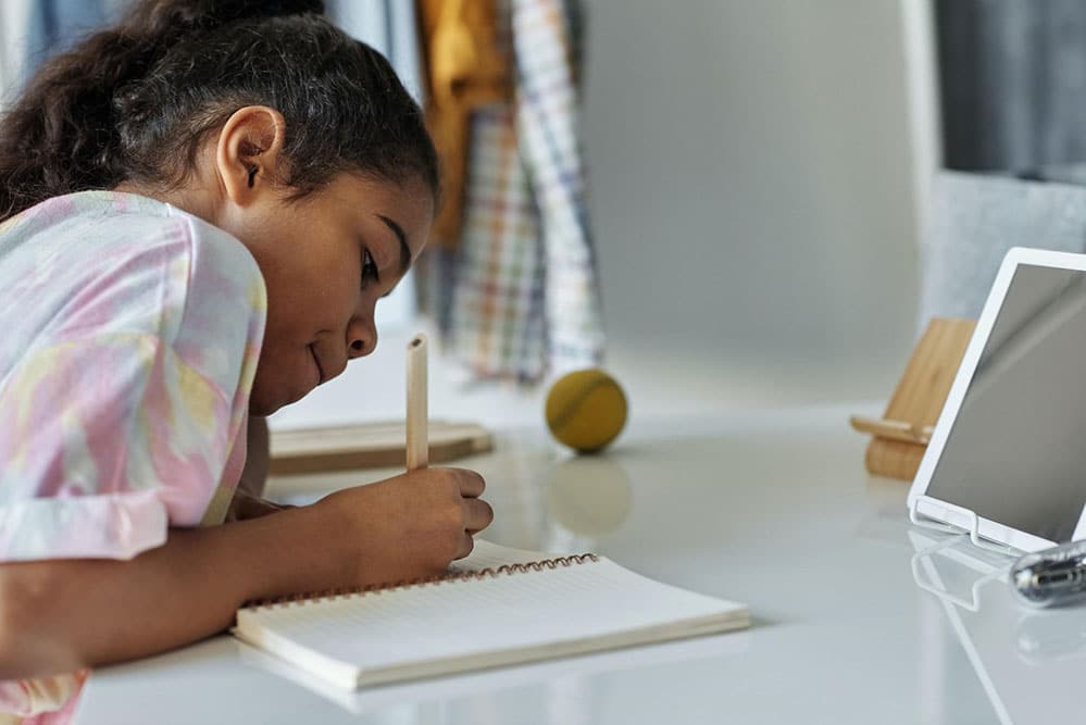 Child sitting at desk with a pencil in their hand writing in a book